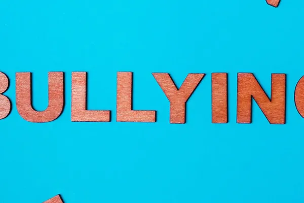 'BULLYING' in wooden letters on a blue background with scattered letters around it.