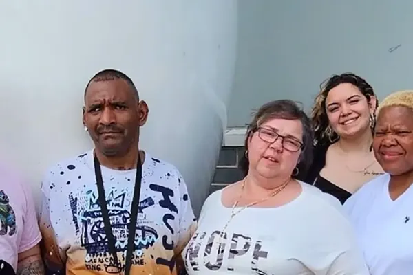 A group of six people standing outside in front of a large white structure, dressed casually.