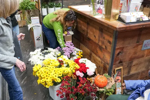 Group of people including a woman in a wheelchair admiring colorful chrysanthemums and fall flowers at a neighborhood florist shop during a community visit