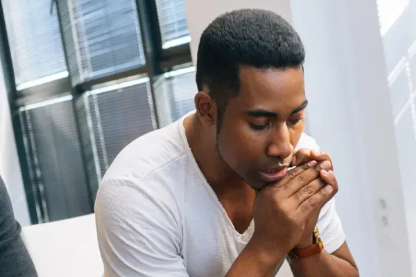 Three people in a quiet, reflective moment together in a bright office space, with the center figure appearing thoughtful while others sit attentively nearby.