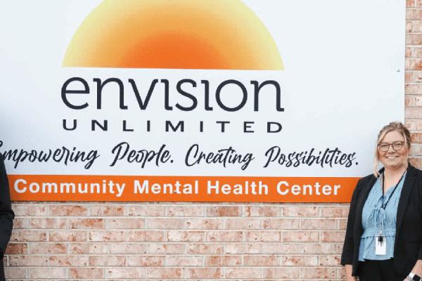 A group of five people stand in front of a sign for Envision Unlimited, a Community Mental Health Center.