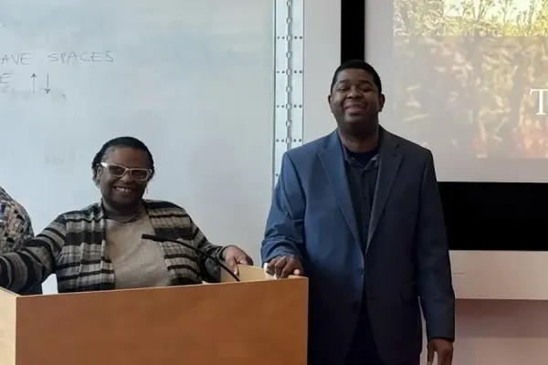 Three people stand by a podium and presentation screen with 'Thank You' displayed.