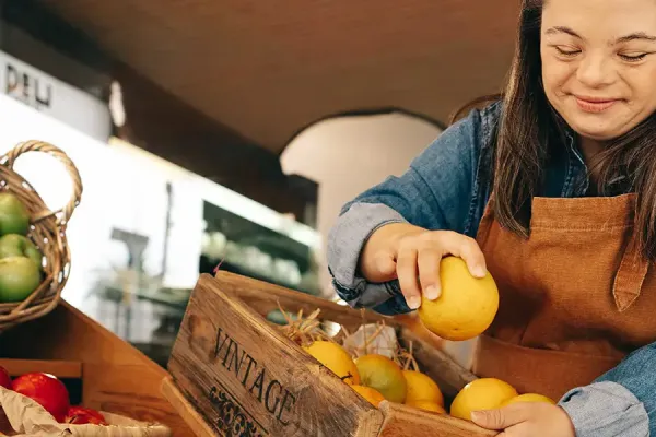 Woman with Down syndrome restocking fresh fruits in the vegetable section of a grocery store.