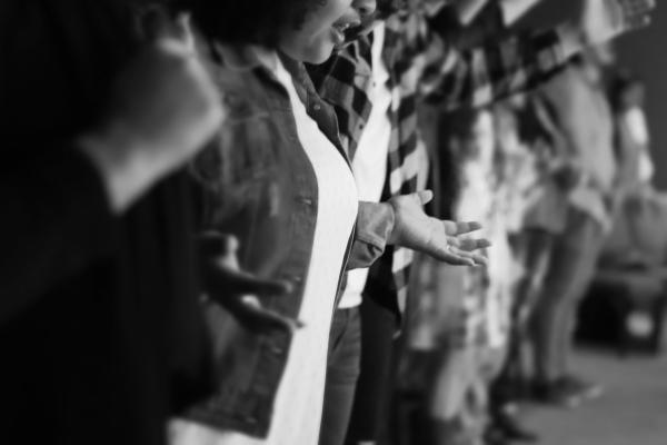 A black and white photo of a group of people standing with their hands lifted and held out.