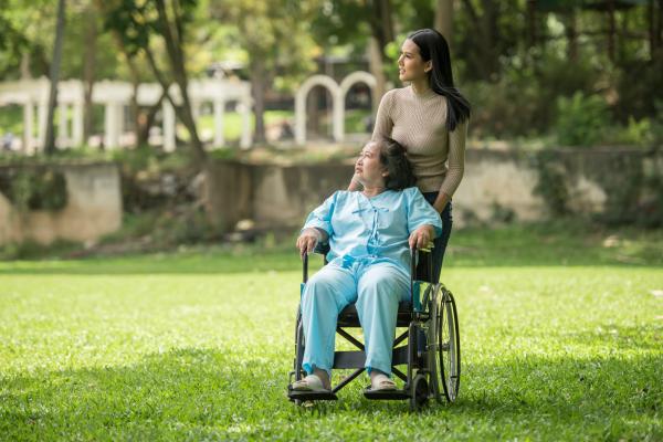 A caregiver guides an individual in a wheelchair on a walk outside