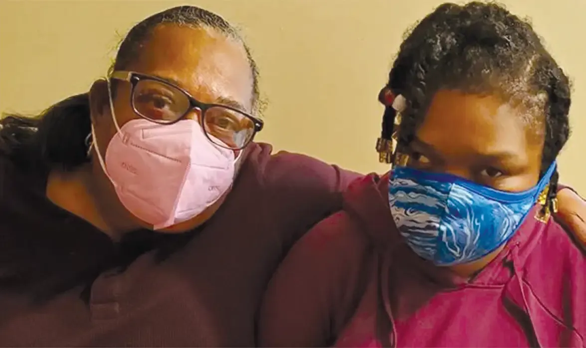 Two people wearing masks pose together for a portrait against a yellow background