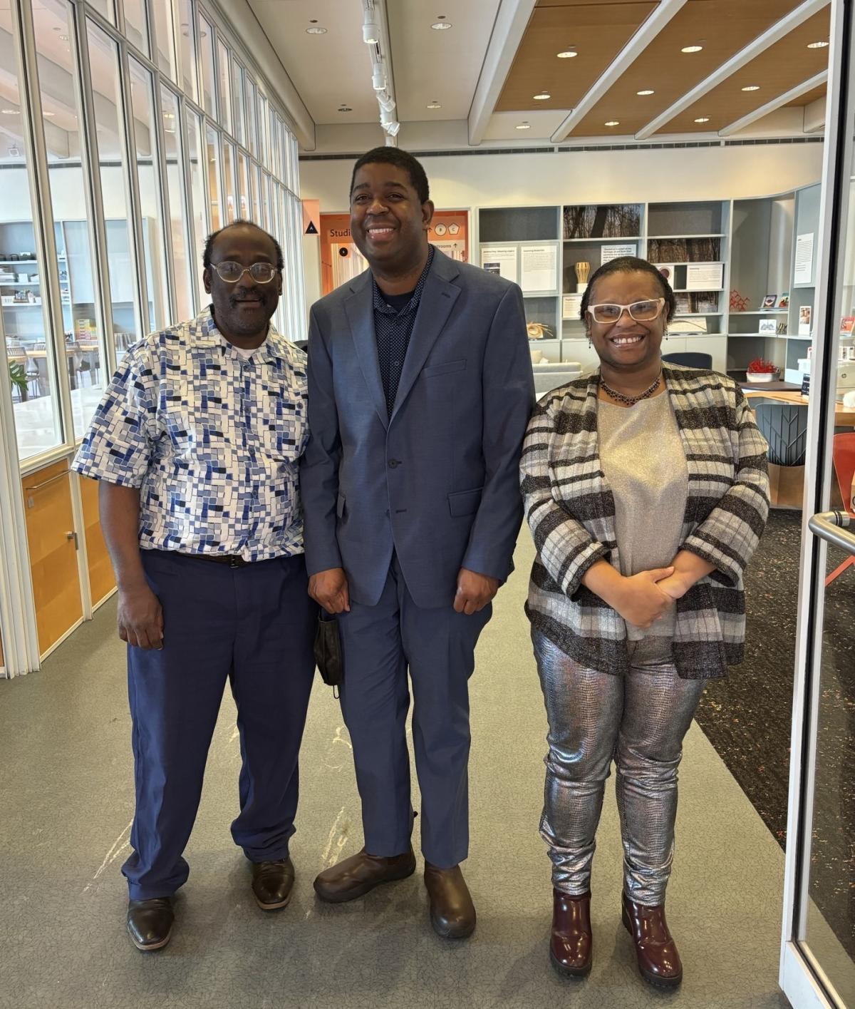 Three people smiling indoors with shelving and displays in the background.