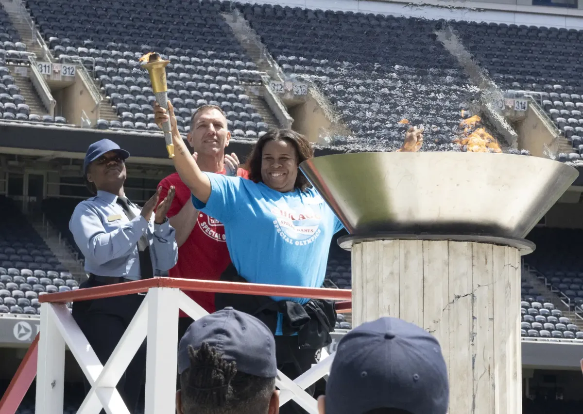 Three people on a platform in a stadium, participating in a torch lighting ceremony.