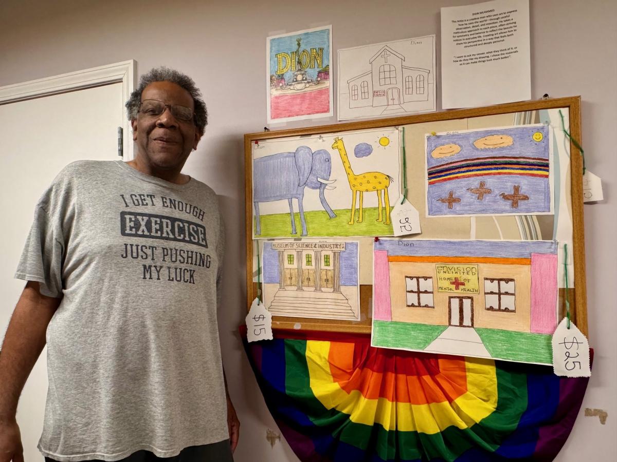 A person standing next to a board with colorful drawings and a rainbow banner.