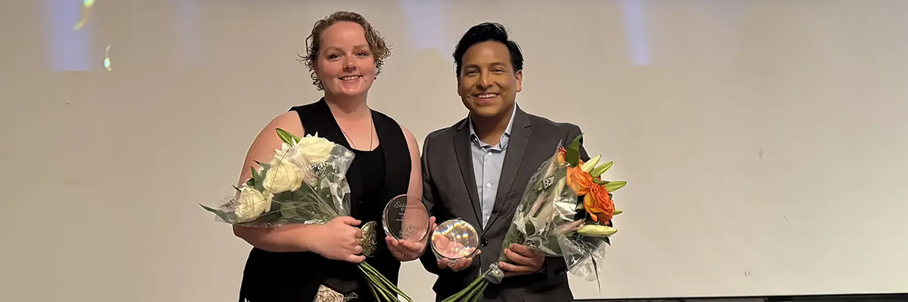 Two professionals holding bouquets and award glasses at The Arc Illinois 'Together, We Rise' Awards Reception event, with the event banner visible behind them.