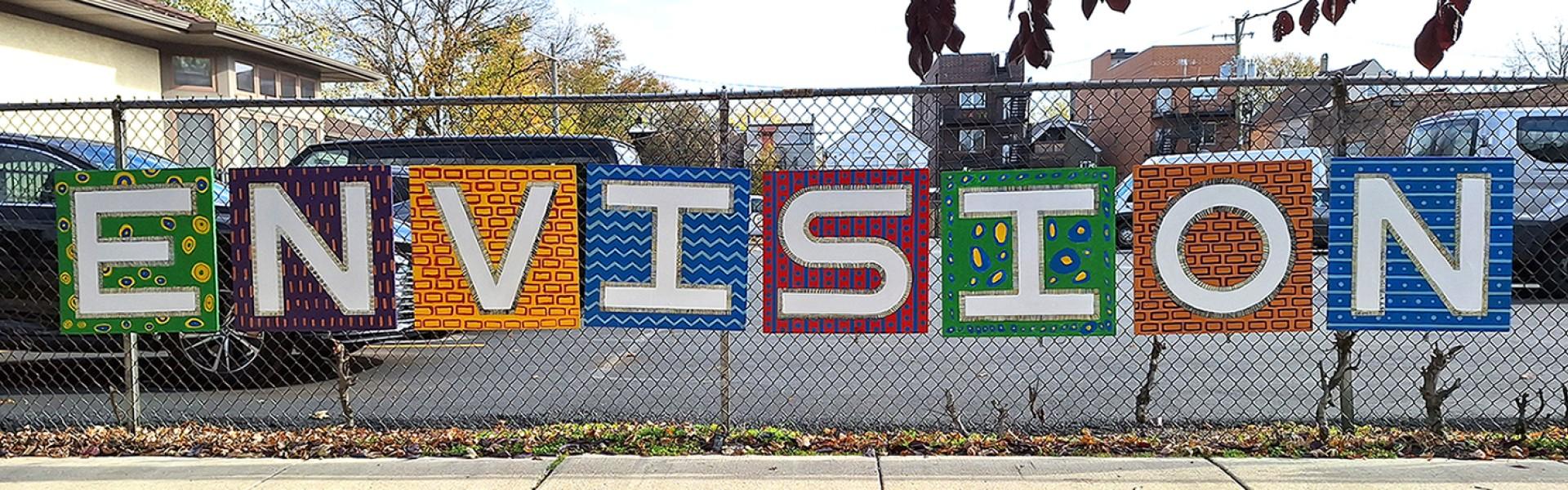 A fence is pictured with the colorful word ENVISION displayed across it