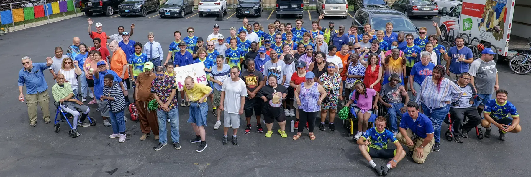Large diverse group of over 100 people wearing blue 'Journey of Hope' shirts gathered in a parking lot, smiling and waving at the camera.