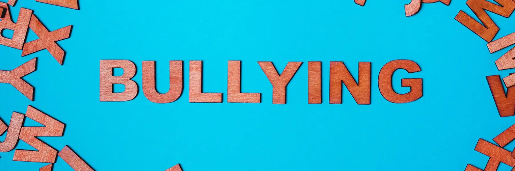 'BULLYING' in wooden letters on a blue background with scattered letters around it.