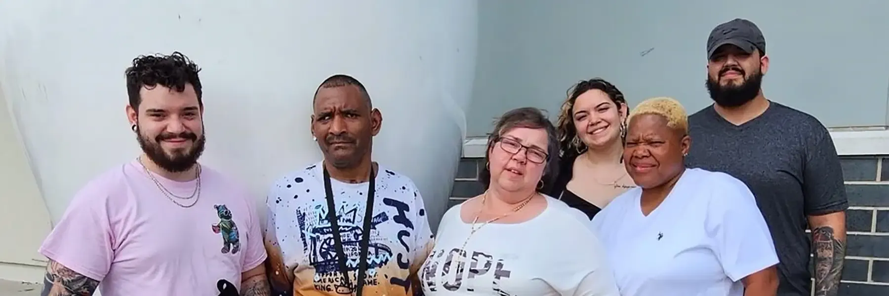 A group of six people standing outside in front of a large white structure, dressed casually.