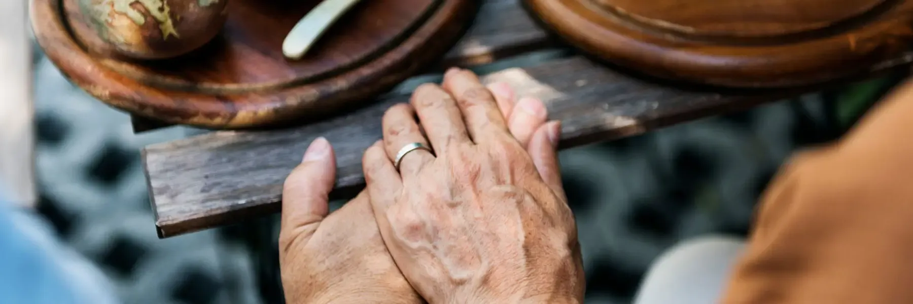 Close-up of hands with a silver ring resting on a wooden table.