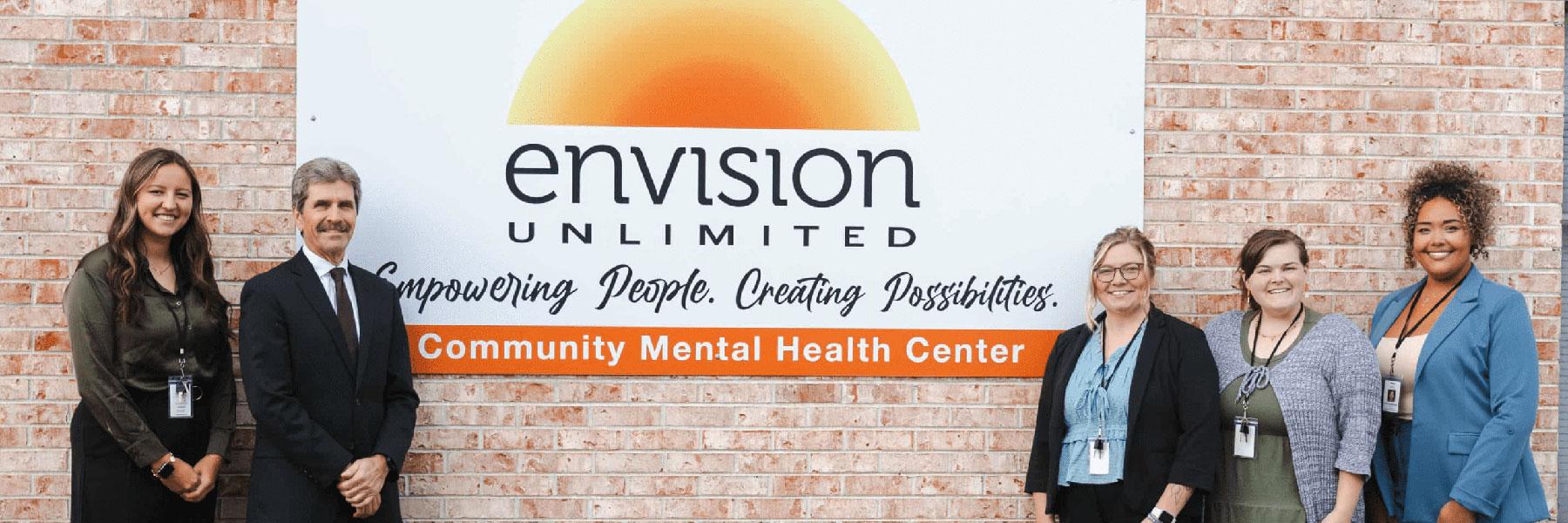 A group of five people stand in front of a sign for Envision Unlimited, a Community Mental Health Center.