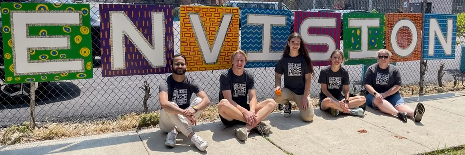 Five people sitting in front of a colorful 'ENVISION' sign.