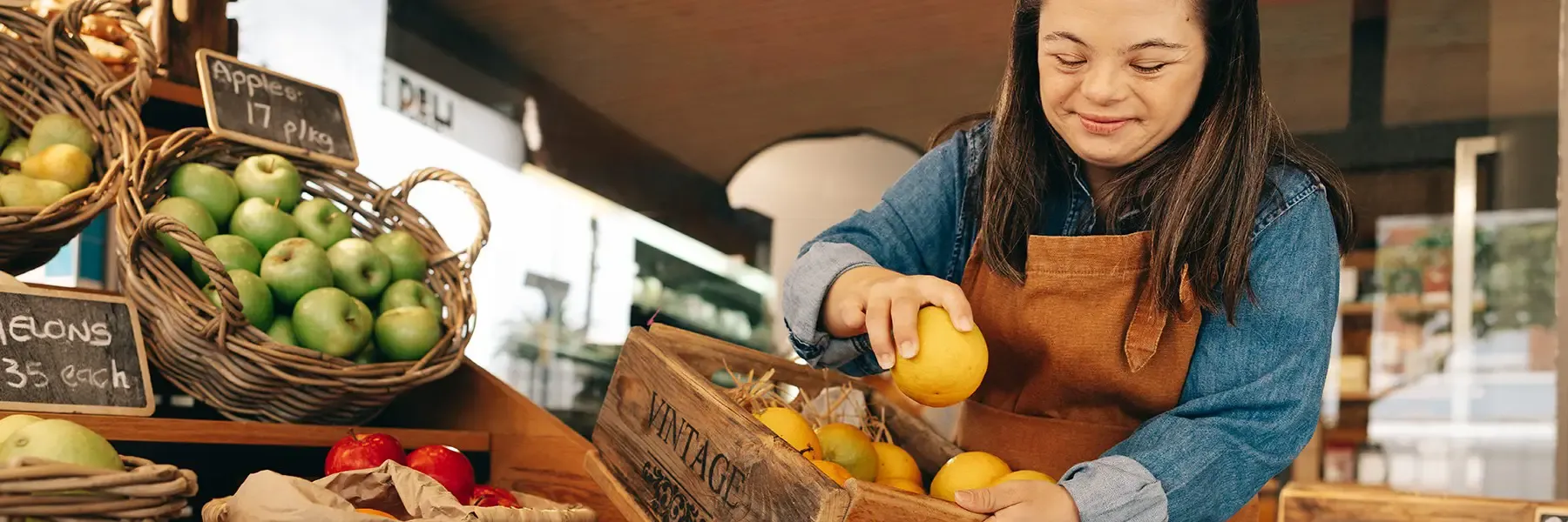 Woman with Down syndrome restocking fresh fruits in the vegetable section of a grocery store.