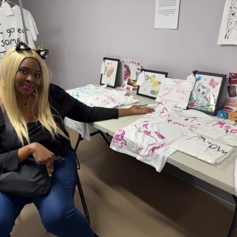 A person sitting next to a table with t-shirts.