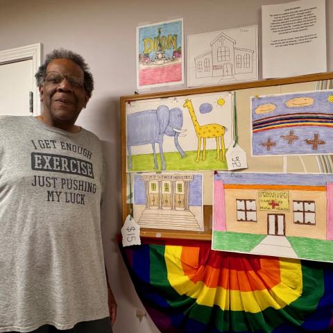 A person standing next to a board with colorful drawings and a rainbow banner.