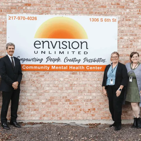 A group of five people stand in front of a sign for Envision Unlimited, a Community Mental Health Center.