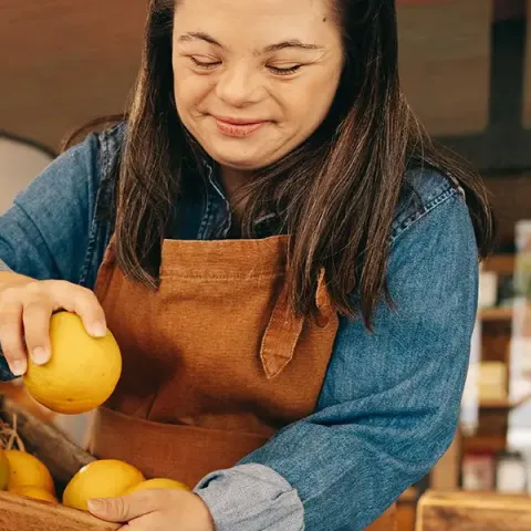 Woman with Down syndrome restocking fresh fruits in the vegetable section of a grocery store.