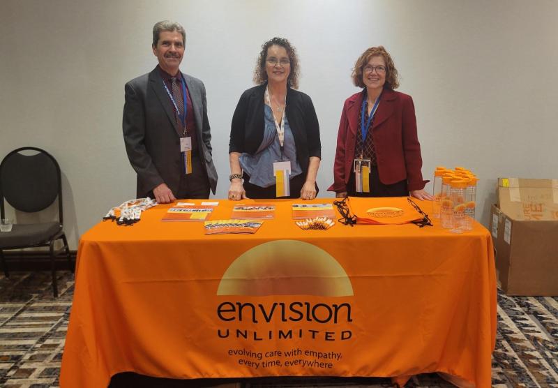 Three Envision Unlimited staff members are pictured at a booth at a local conference