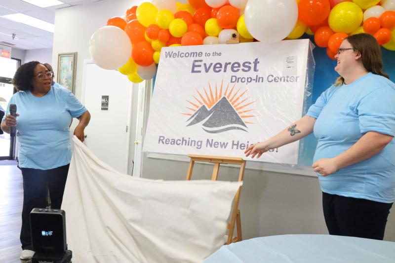Two Envision Unlimited staff members reveal signage for the Everest drop-in center in a celebratory fashion, with balloons in the background