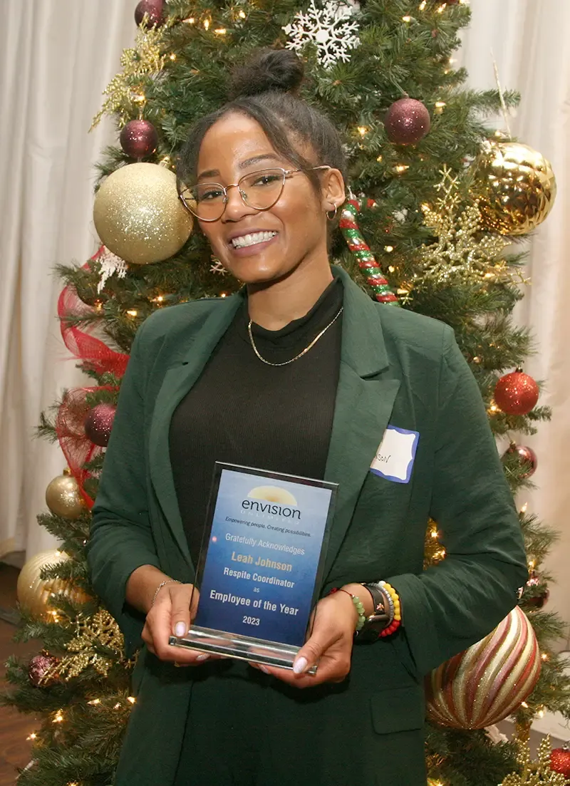 A person holding an award stands in front of a decorated Christmas tree.